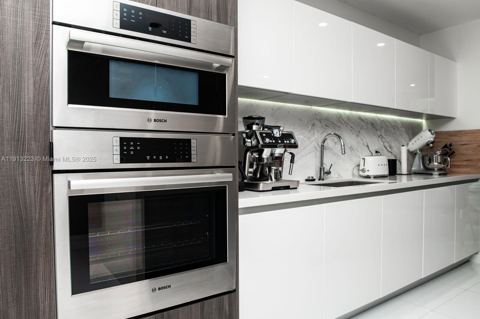 A modern kitchen features stainless steel Bosch wall ovens, white cabinetry, and marble countertops — 851 NE 1st Ave # 1811, Miami FL 33132, MIAMI, FL