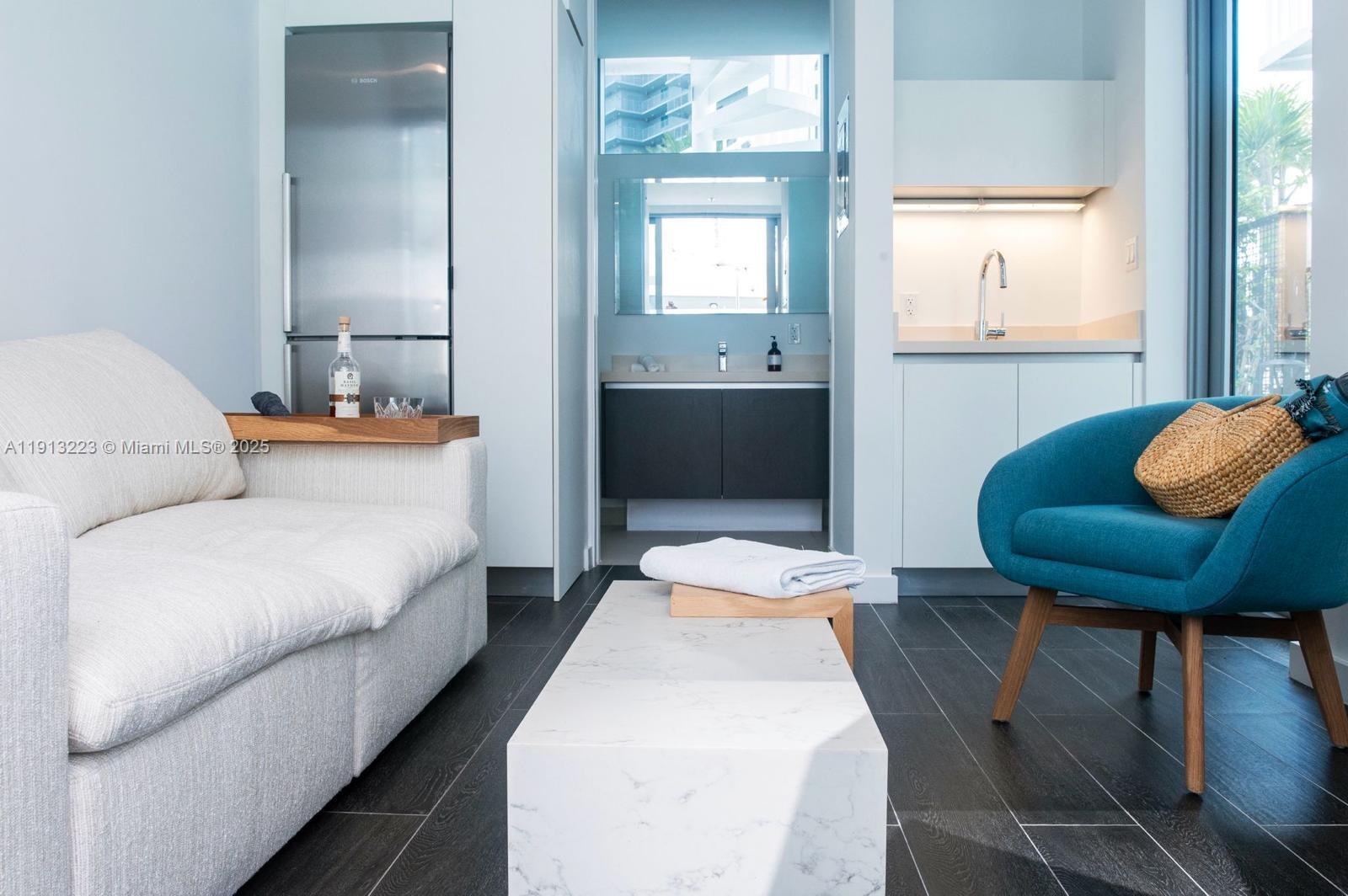 A modern studio apartment features a sofa, a blue armchair, a kitchenette, and a bathroom — 851 NE 1st Ave # 1811, Miami FL 33132, MIAMI, FL