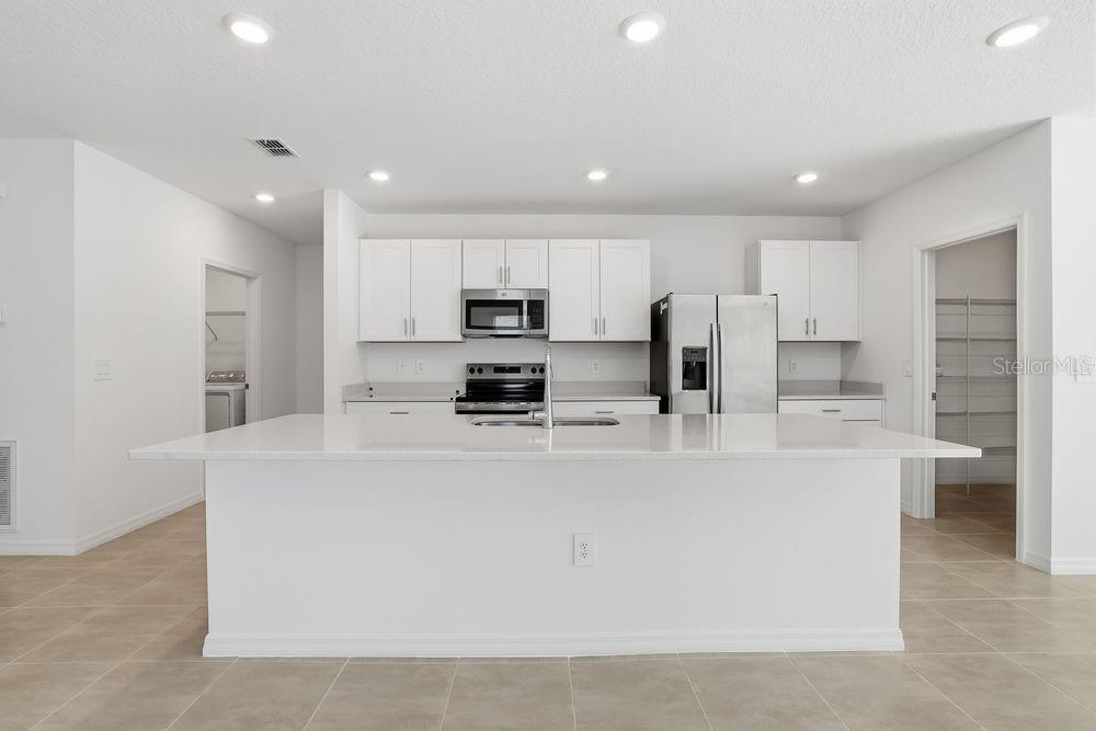 A modern kitchen features white cabinets, stainless steel appliances, and a large central island — 13673 TROPICAL BREEZE WAY, HUDSON, FL