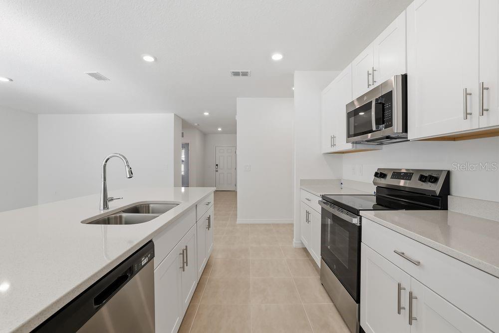 A modern kitchen features white cabinets, quartz countertops, stainless steel appliances, and a central island — 13673 TROPICAL BREEZE WAY, HUDSON, FL