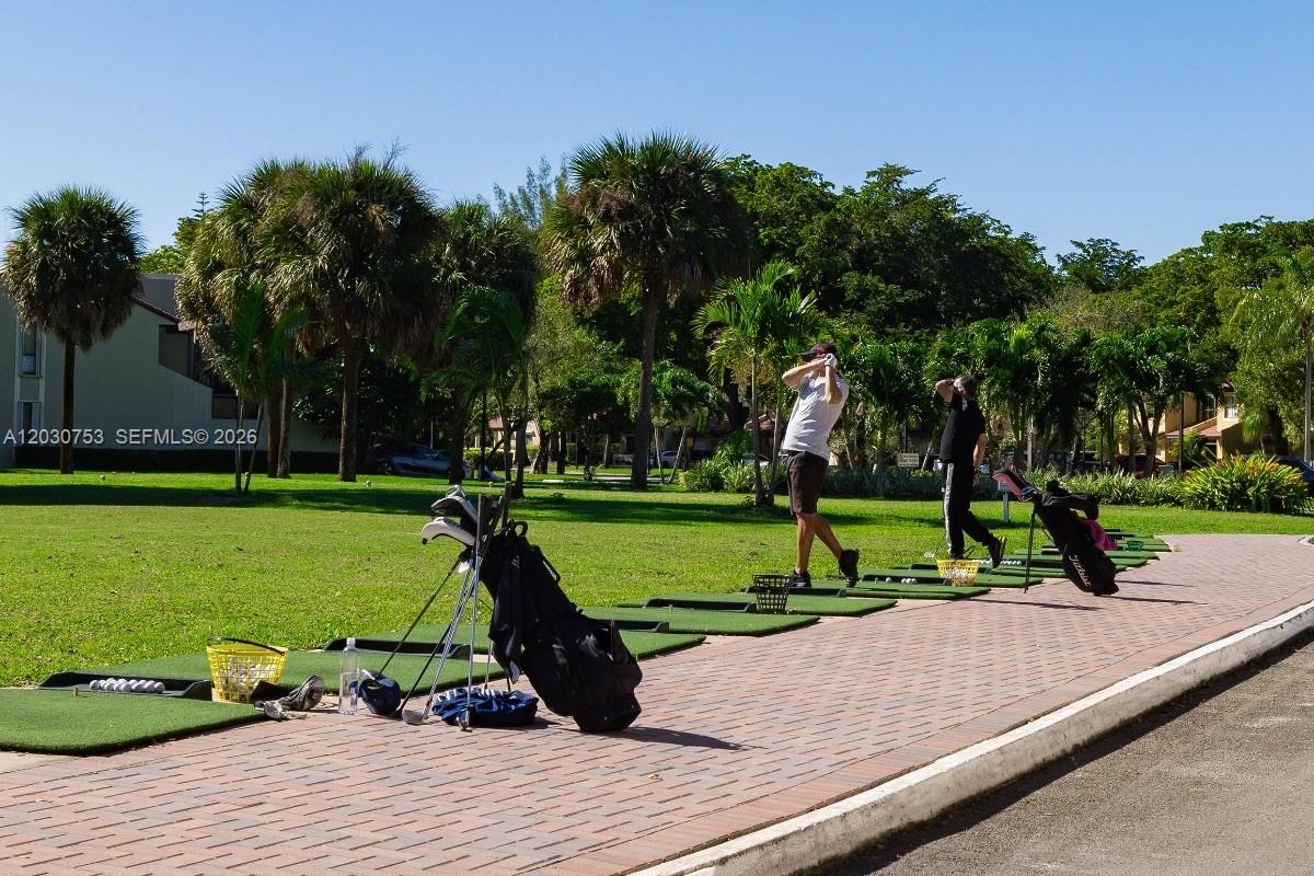 Two people practice their golf swings at an outdoor driving range with palm trees — 3932 Estepona Ave, Doral FL 33178, DORAL, FL