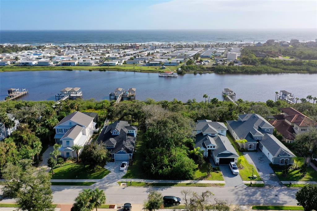 An aerial view shows four houses near a river with a beach community in the background — 41 S RIVERWALK DRIVE, PALM COAST, FL