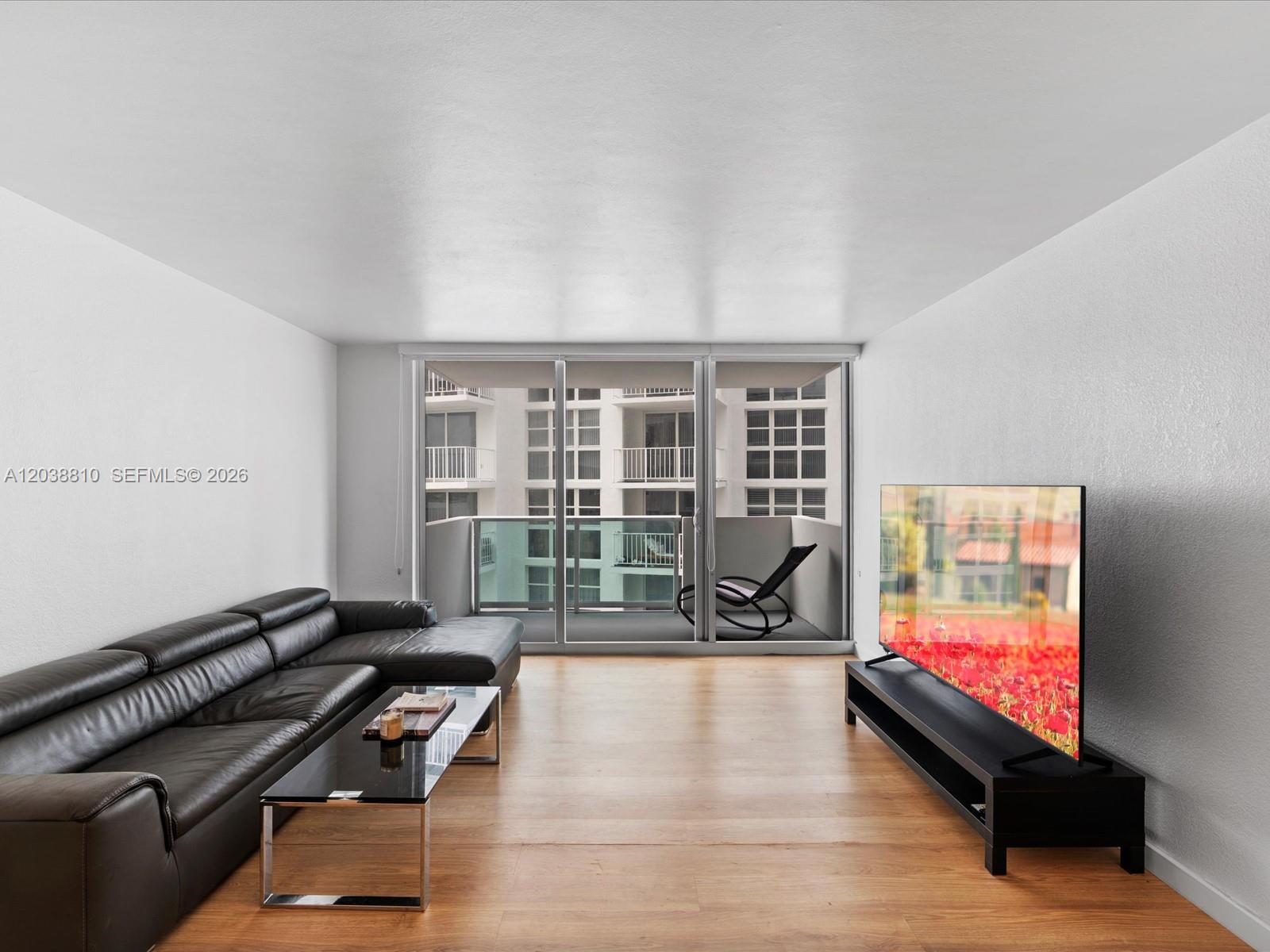 A living room features a black leather sectional, glass coffee table, and a balcony view — 1200 West Ave # 823, Miami Beach FL 33139, MIAMI BEACH, FL