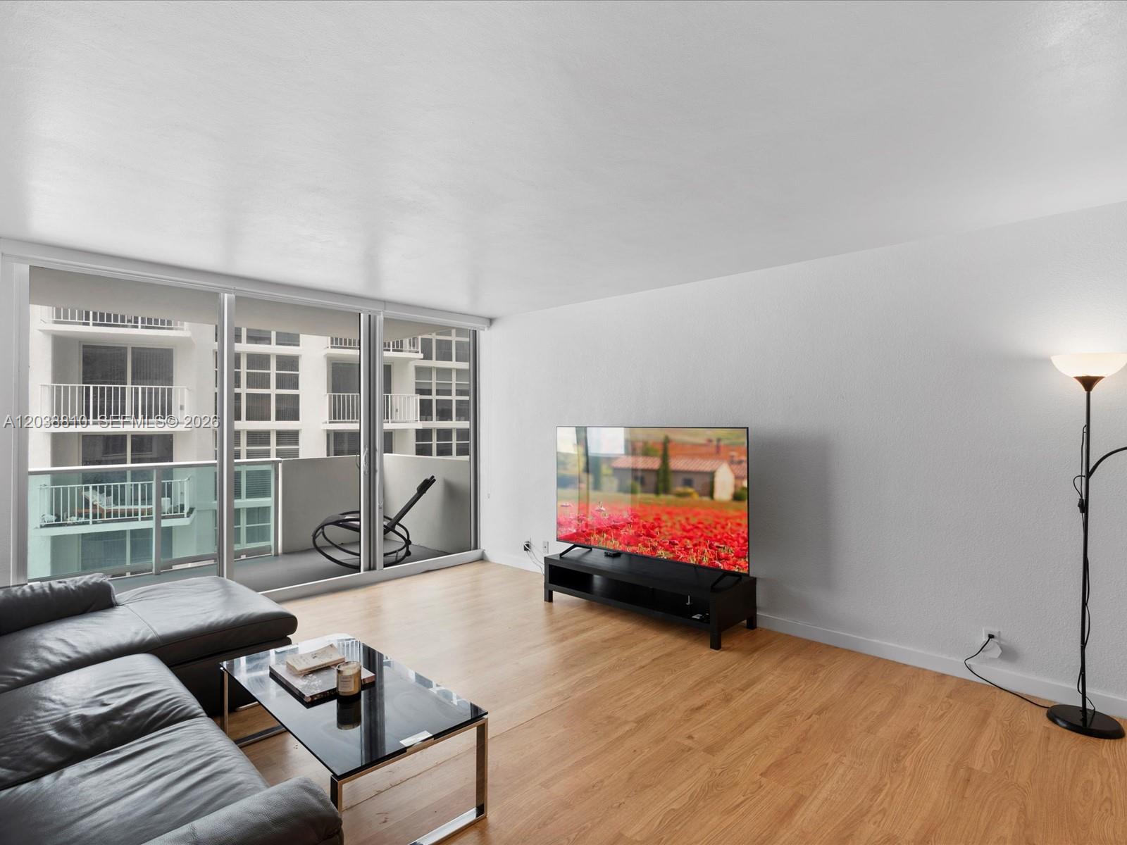 A living room features light wood flooring, a black leather sofa, and a balcony view — 1200 West Ave # 823, Miami Beach FL 33139, MIAMI BEACH, FL
