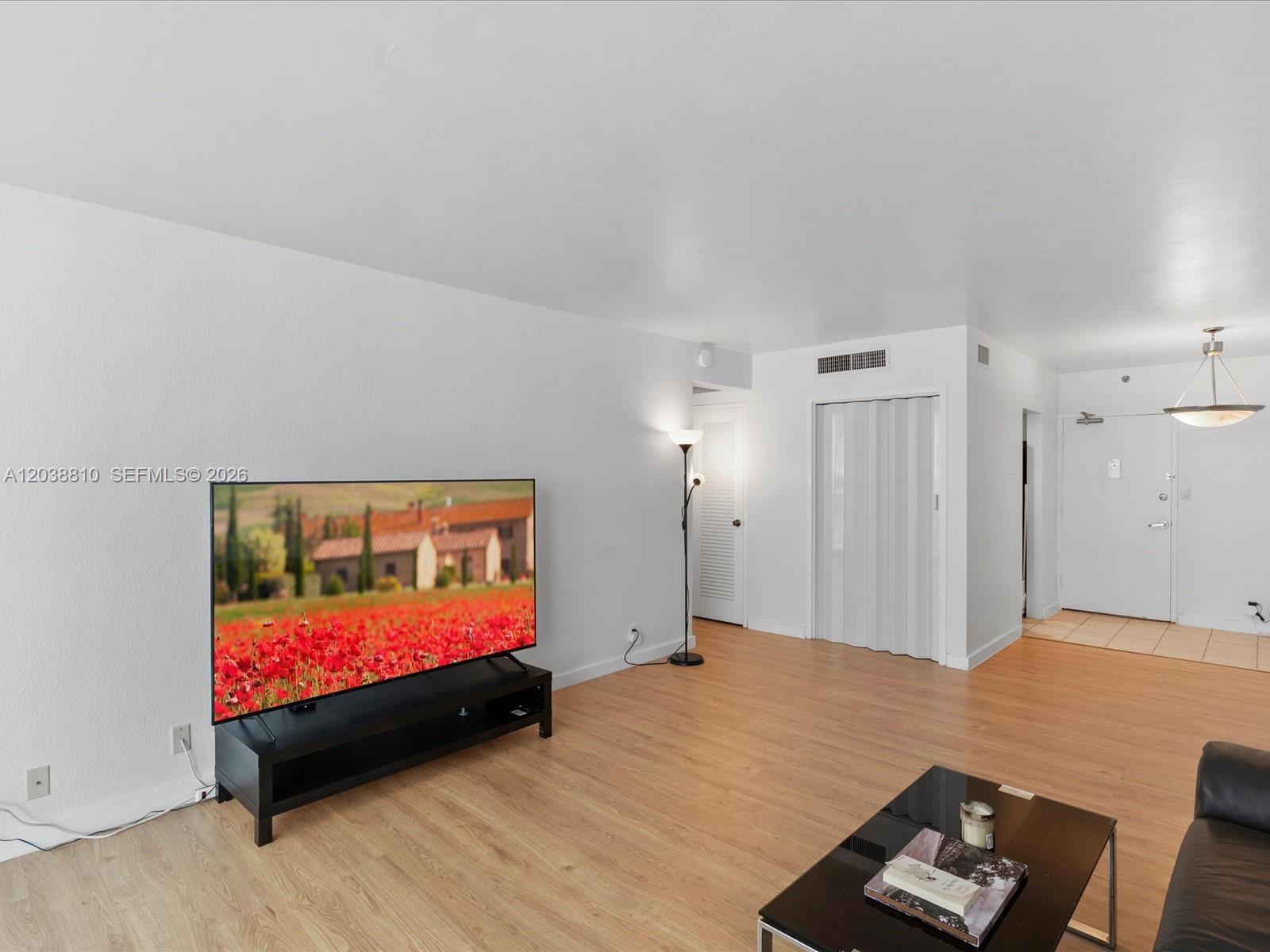 A living room features light wood-look flooring, a television on a stand, and white walls — 1200 West Ave # 823, Miami Beach FL 33139, MIAMI BEACH, FL