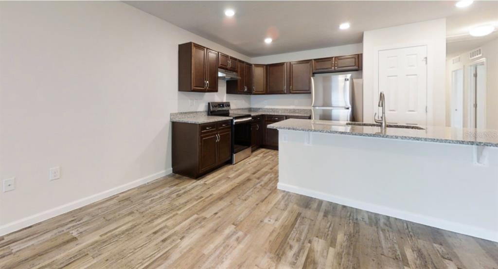 A kitchen with dark wood cabinets, granite countertops, stainless steel appliances, and wood-look flooring — 18 SECOND PATH UNIT A & B, PALM COAST, FL