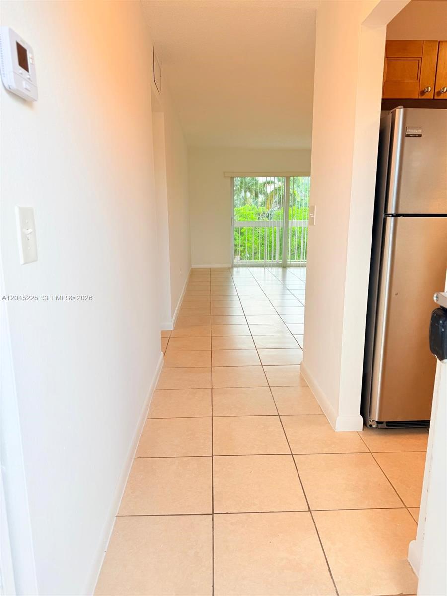 A tiled hallway leads past a stainless steel refrigerator toward a sliding glass balcony door — 7705 Camino Real # B413, Miami FL 33143, MIAMI, FL