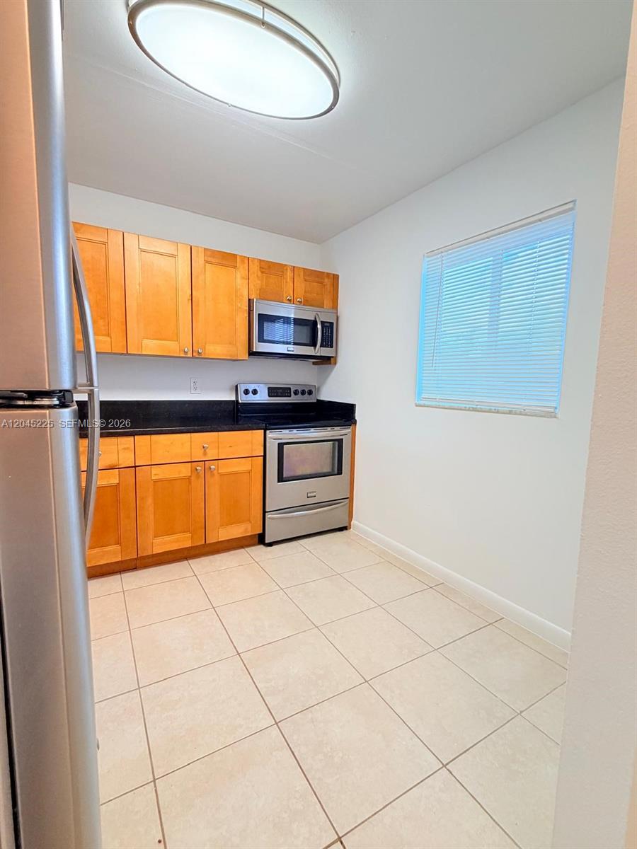 A kitchen features light wood cabinets, stainless steel appliances, dark countertops, and tile flooring — 7705 Camino Real # B413, Miami FL 33143, MIAMI, FL