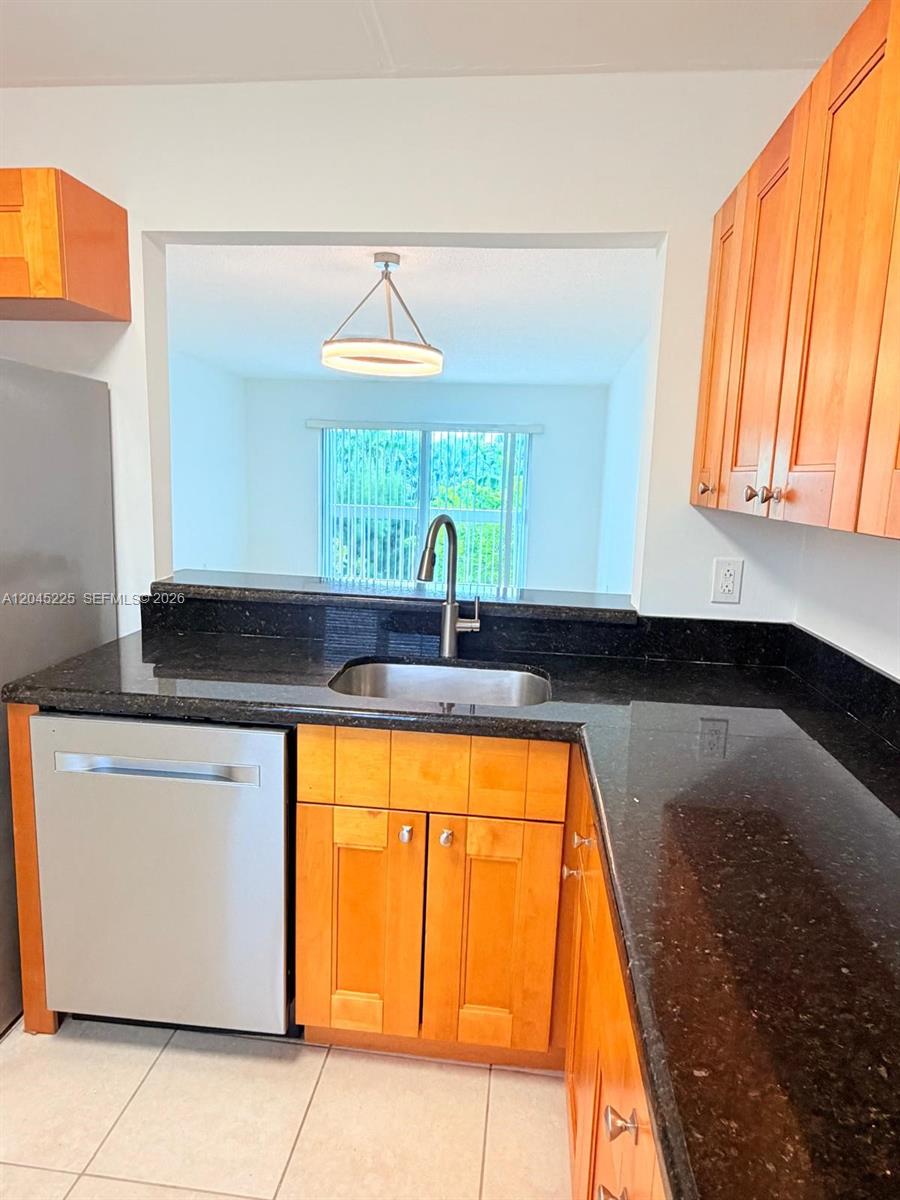 A kitchen features wood cabinets, black granite countertops, a stainless steel dishwasher, and a sink — 7705 Camino Real # B413, Miami FL 33143, MIAMI, FL