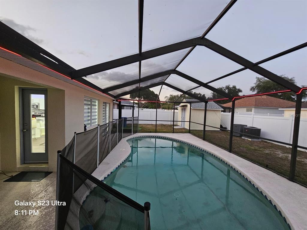 A screened-in pool enclosure features a kidney-shaped pool, a safety fence, and LED lighting — 2256 TOWERING OAKS CIRCLE, SEFFNER, FL