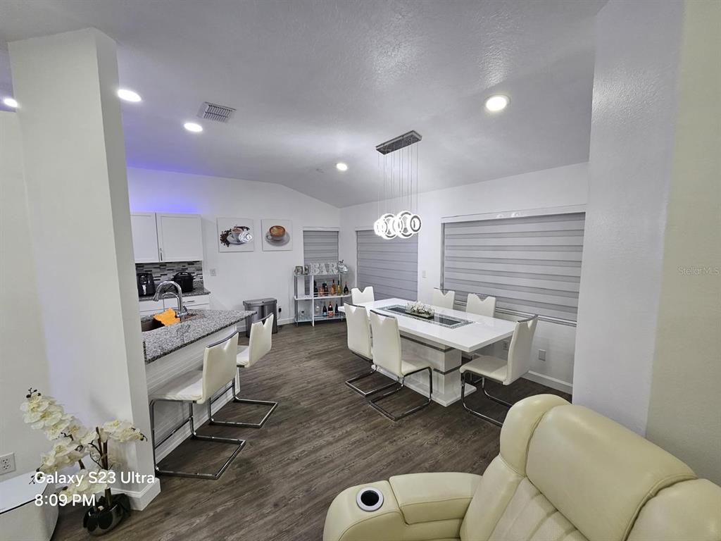A modern dining area with a white table, six chairs, and an adjacent kitchen island — 2256 TOWERING OAKS CIRCLE, SEFFNER, FL