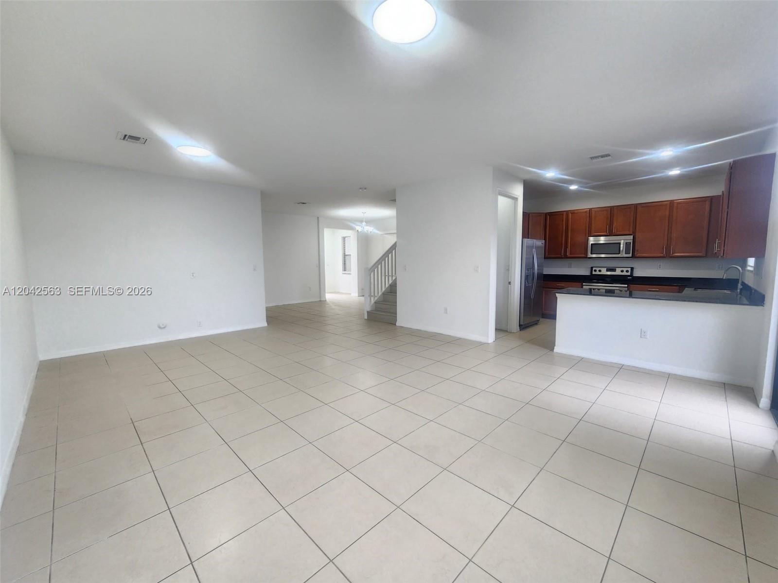 An open-concept living area features light tile flooring, white walls, and a kitchen with wood cabinets — MIAMI, FL