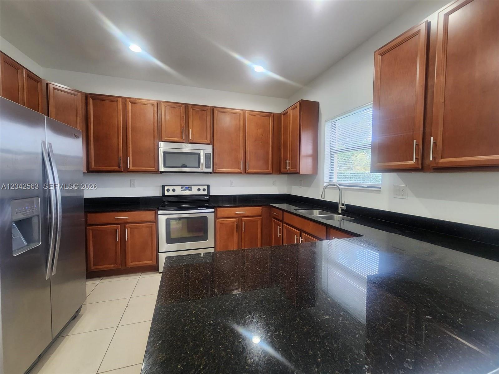 A kitchen features wood cabinets, black granite countertops, and stainless steel appliances — MIAMI, FL