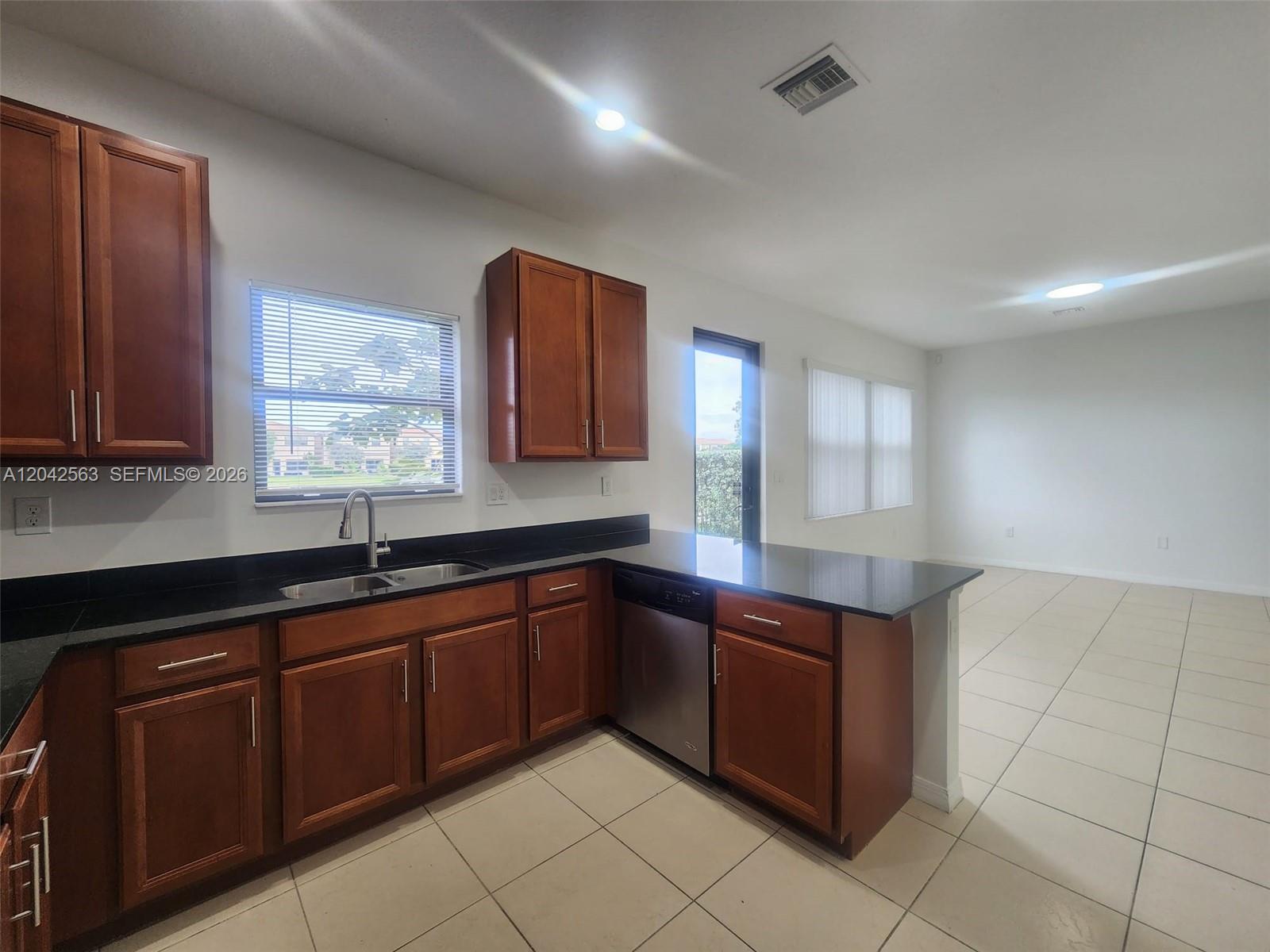 A kitchen features dark wood cabinets, black countertops, stainless steel appliances, and tile flooring — MIAMI, FL