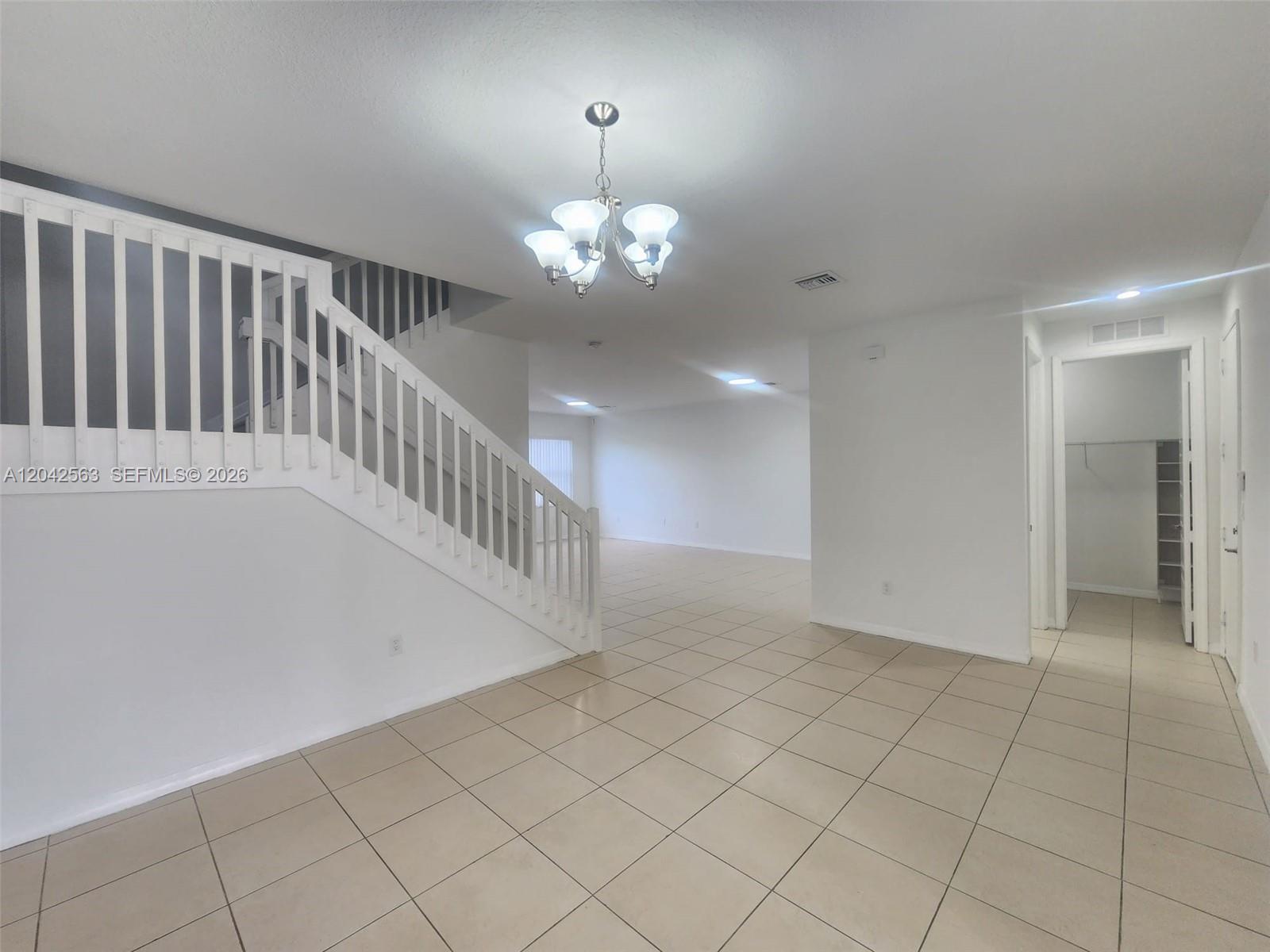 An interior view shows a tiled room with a white staircase and a chandelier — MIAMI, FL