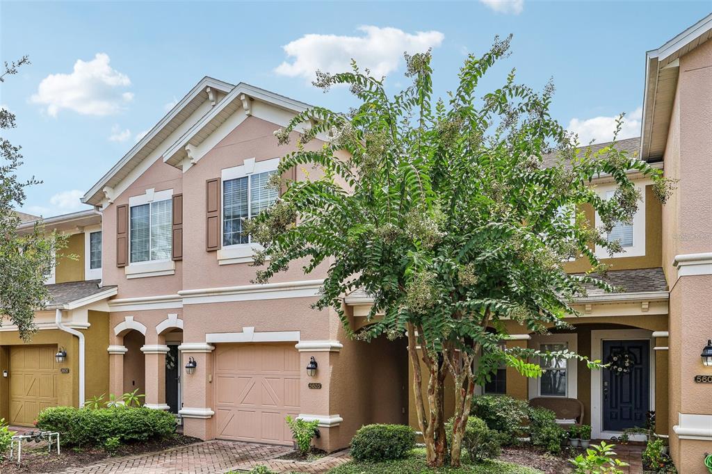 A two-story townhouse with a tan stucco exterior, a single-car garage, and a large tree — 5605 RUTHERFORD PLACE, OVIEDO, FL