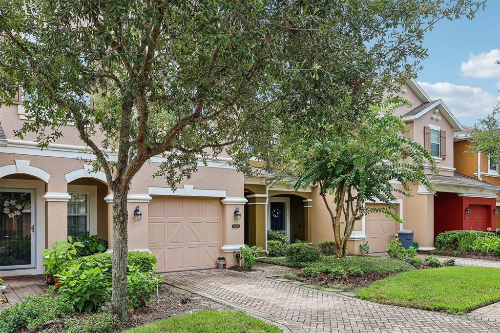 A two-story townhouse with a tan stucco exterior, a brick paver driveway, and mature trees — 5605 RUTHERFORD PLACE, OVIEDO, FL