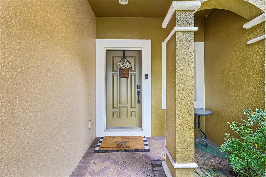 A covered entryway features a tan door with a hanging basket and a brick floor — 5605 RUTHERFORD PLACE, OVIEDO, FL