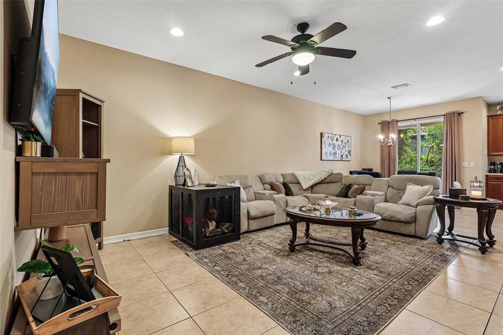A living room features a beige sectional sofa, a dog crate, and tile flooring — 5605 RUTHERFORD PLACE, OVIEDO, FL
