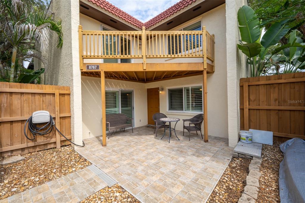A paved patio sits beneath a wooden balcony attached to a two-story stucco building — 8767 LIVE OAK COURT, CAPE CANAVERAL, FL