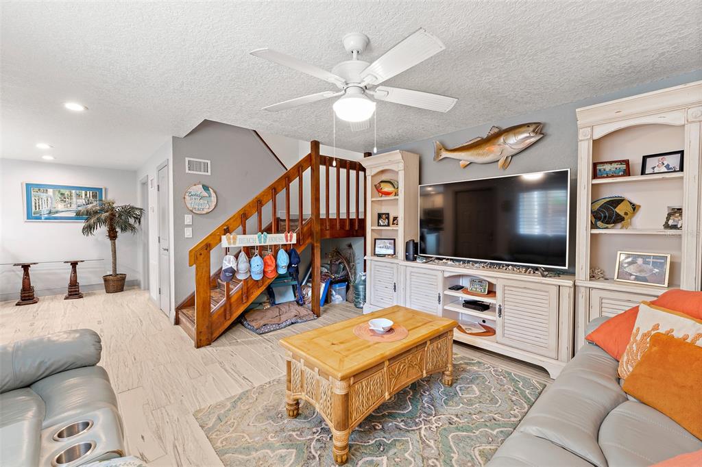A living room features a wooden staircase, a large television, and a light-colored tile floor — 8767 LIVE OAK COURT, CAPE CANAVERAL, FL