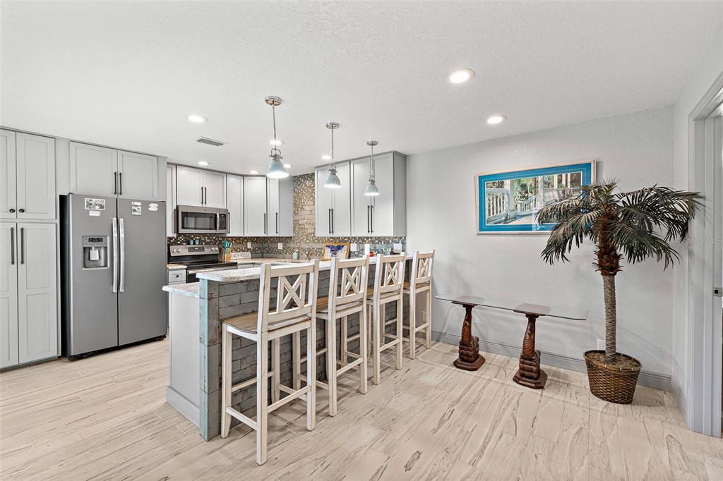 A kitchen features light gray cabinetry, a stone-accented breakfast bar with four stools, and wood-look flooring — 8767 LIVE OAK COURT, CAPE CANAVERAL, FL