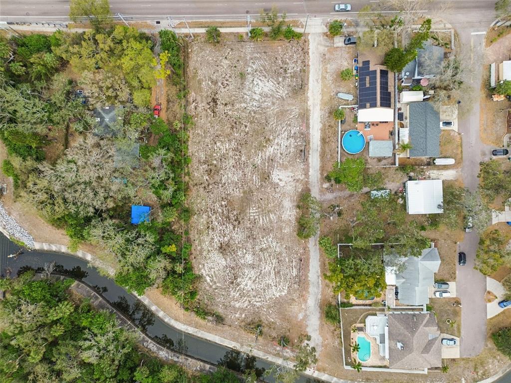 An aerial view shows a vacant, rectangular lot bordered by trees, a canal, and houses — 5306 73RD WAY N, ST PETERSBURG, FL