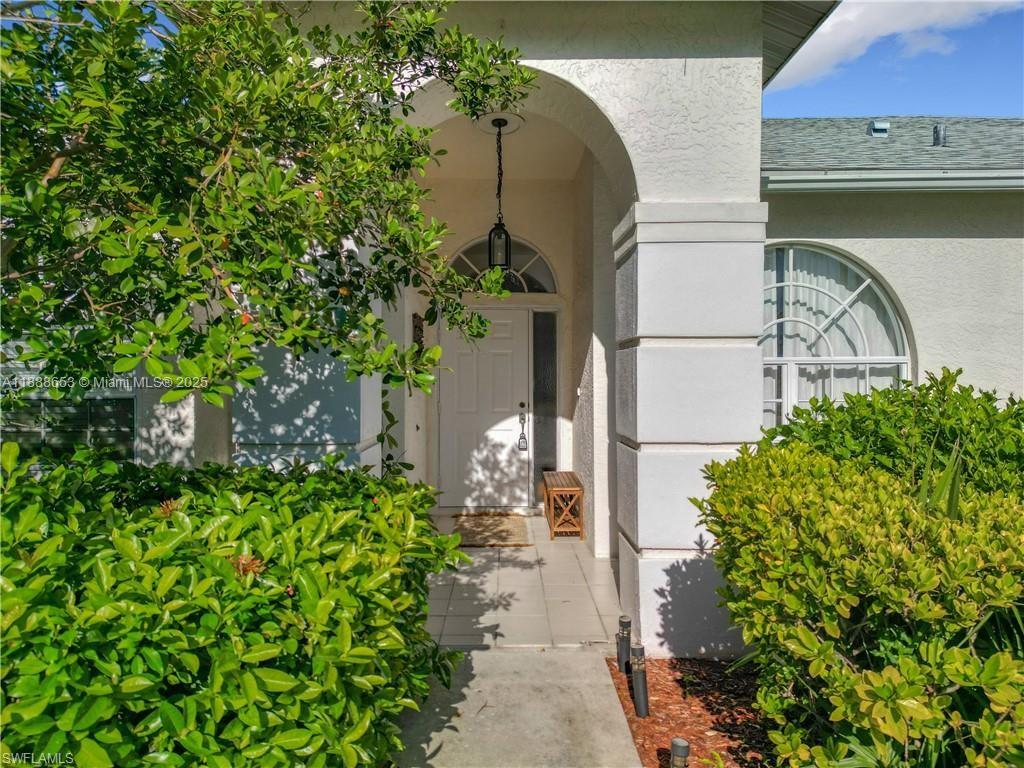 The exterior of a house features a white arched entryway, a front door, and landscaping — 4991 Brixton Ct, Naples FL 34104, NAPLES, FL