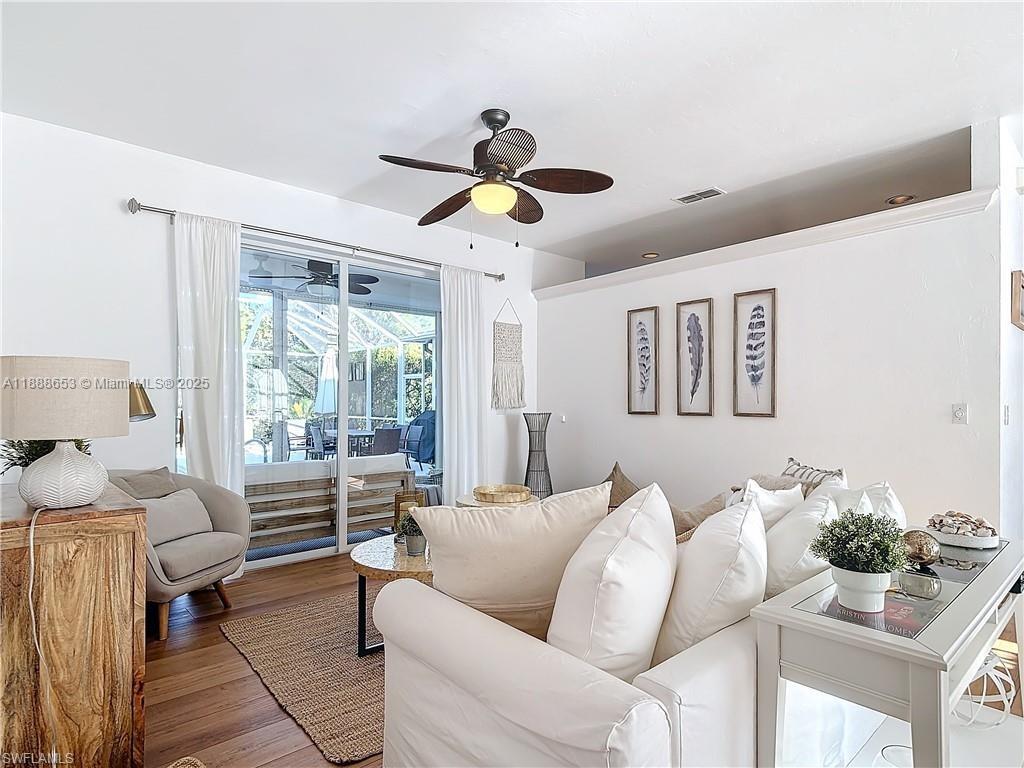 A bright living room features white sofas, a ceiling fan, and sliding doors to a patio — 4991 Brixton Ct, Naples FL 34104, NAPLES, FL