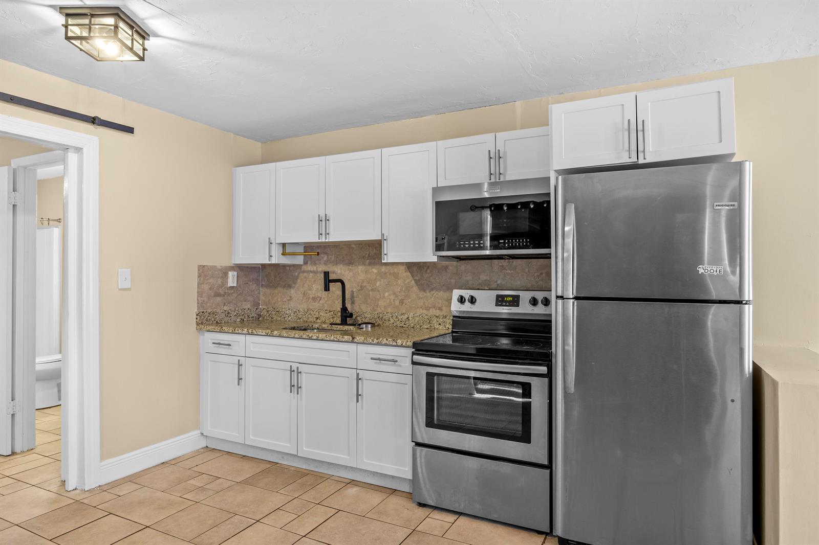 A kitchen features white cabinets, stainless steel appliances, granite countertops, and light-colored tile flooring — 120 Pleasant Place # 1, Palm Springs FL 33461, PALM SPRINGS, FL