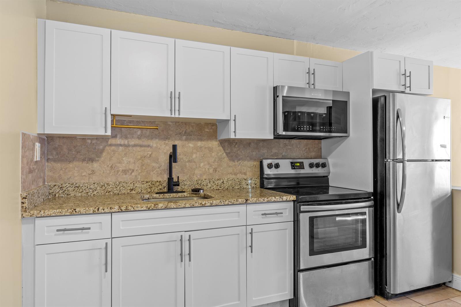 A kitchen features white cabinets, granite countertops, stainless steel appliances, and a tiled backsplash — 120 Pleasant Place # 1, Palm Springs FL 33461, PALM SPRINGS, FL