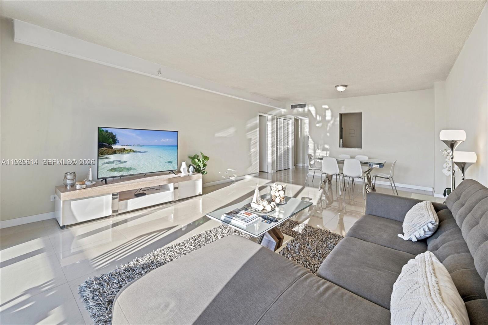A living room features a grey sectional sofa, a glass coffee table, and a television console — 5601 Collins Ave # 1618, Miami Beach FL 33140, MIAMI BEACH, FL