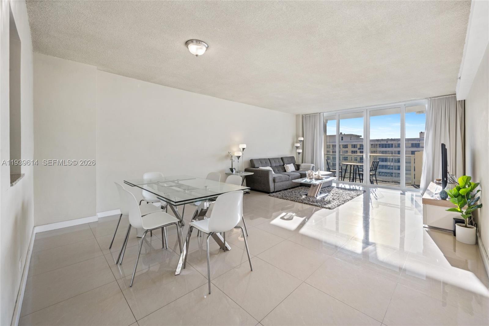 A bright living and dining area with tile floors, a glass table, and balcony access — 5601 Collins Ave # 1618, Miami Beach FL 33140, MIAMI BEACH, FL
