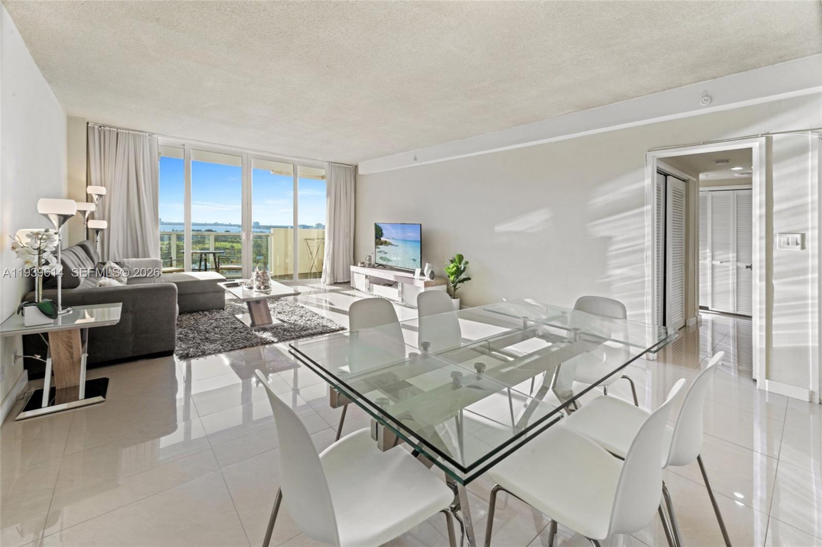 A bright living and dining area features white tile floors, a glass table, and balcony views — 5601 Collins Ave # 1618, Miami Beach FL 33140, MIAMI BEACH, FL