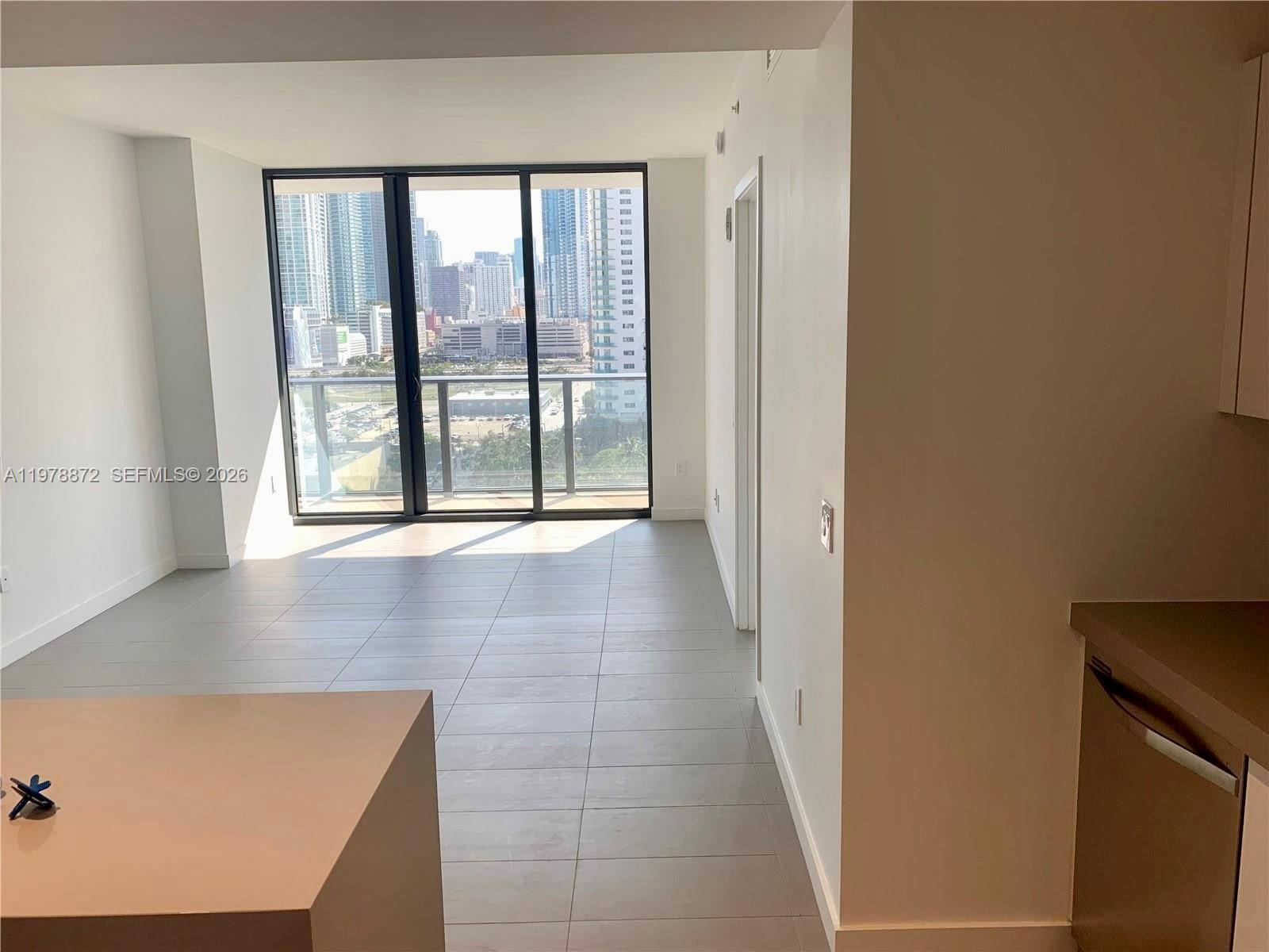 A modern apartment living area features gray tile flooring, white walls, and a balcony view — 1600 NE 1st Ave # 1008, Miami FL 33132, MIAMI, FL