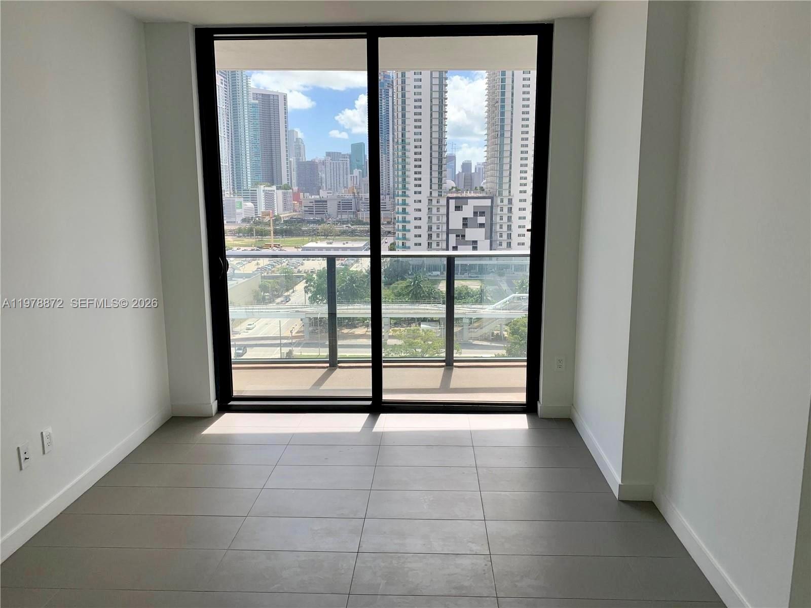 A room with gray tile flooring and a sliding glass door overlooking a city skyline — 1600 NE 1st Ave # 1008, Miami FL 33132, MIAMI, FL