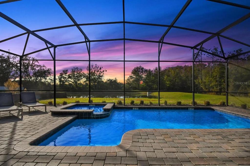 A screened-in pool and spa overlook a grassy yard and pond at sunset — 2721 BOOKMARK DRIVE, KISSIMMEE, FL
