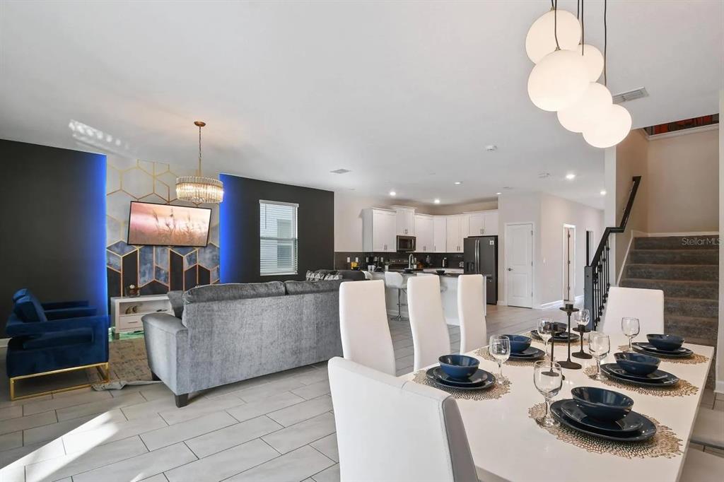 An open-concept living and dining area features a modern accent wall, white cabinetry, and tile flooring — 2721 BOOKMARK DRIVE, KISSIMMEE, FL