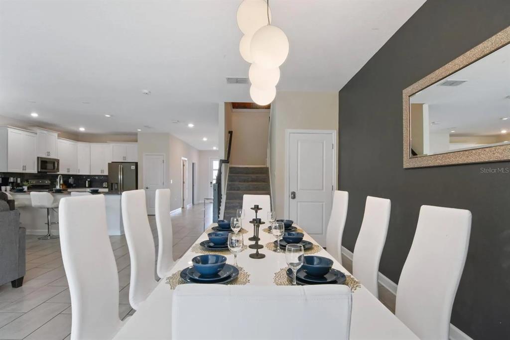 A dining room features a white table with blue place settings and a modern chandelier — 2721 BOOKMARK DRIVE, KISSIMMEE, FL