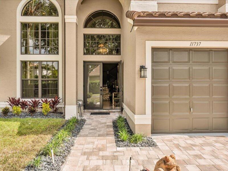 The exterior of a beige house features a paved walkway, a garage, and arched windows — 11737 Preservation Lane, Boca Raton FL 33498, BOCA RATON, FL