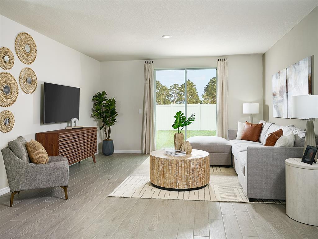 A living room features a grey sectional sofa, wood coffee table, and a wall-mounted television — 1518 BREKEY WAY, ZEPHYRHILLS, FL