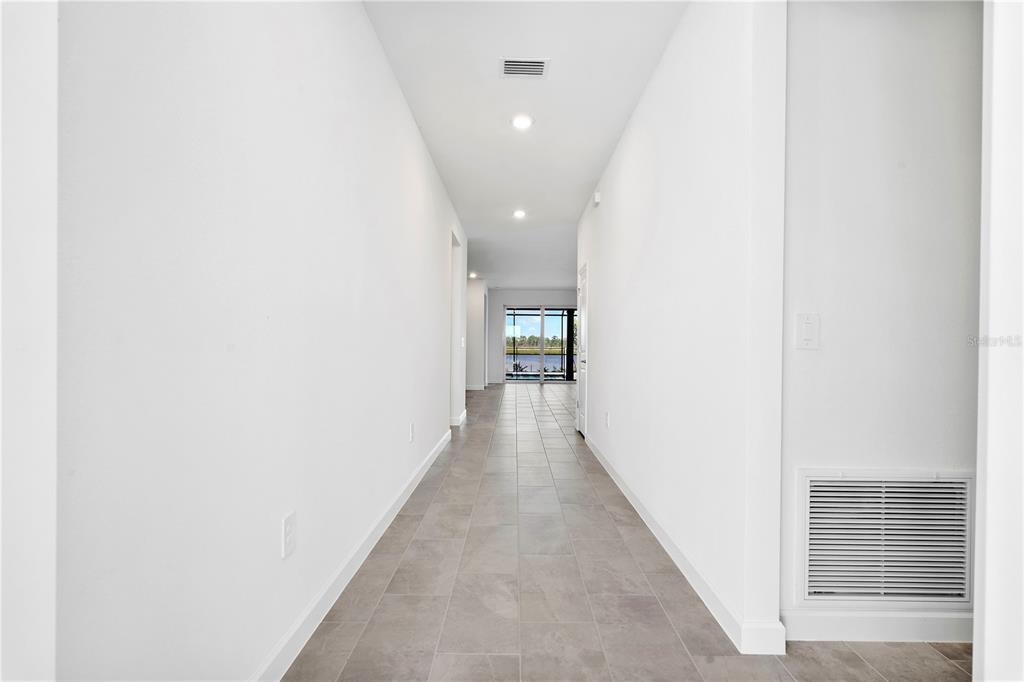 A long, white-walled hallway with gray tile flooring leads toward a glass sliding door — 14735 BLUEWATER ROAD, PUNTA GORDA, FL