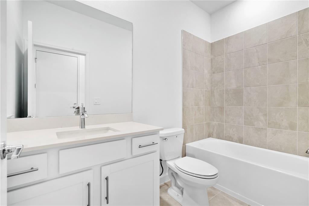 A bathroom features a white vanity with a quartz countertop, a toilet, and a tiled tub — 14735 BLUEWATER ROAD, PUNTA GORDA, FL
