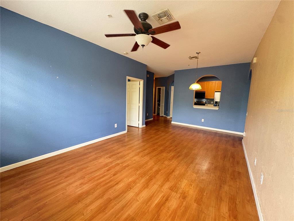 An empty living room features blue walls, wood-look flooring, a ceiling fan, and a kitchen pass-through — 3190 DANTE DRIVE UNIT 307, ORLANDO, FL