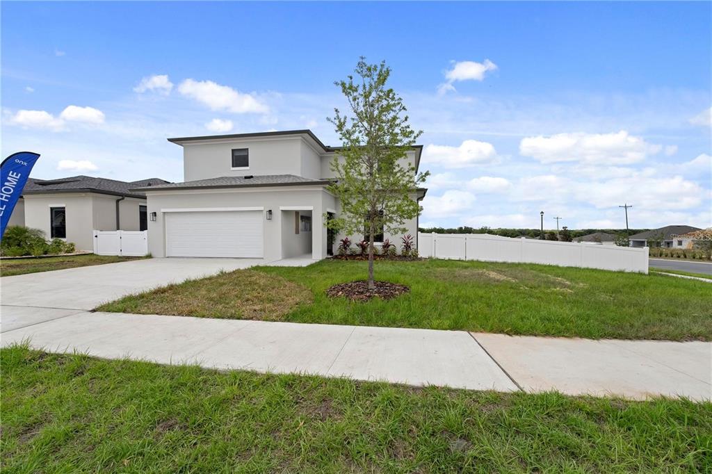 A two-story, light-colored suburban house with a two-car garage and a white vinyl fence — 6390 CHORUS DRIVE, MASCOTTE, FL