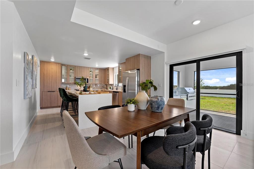 A modern kitchen and dining area with wood cabinetry, a white island, and sliding glass doors — 6390 CHORUS DRIVE, MASCOTTE, FL