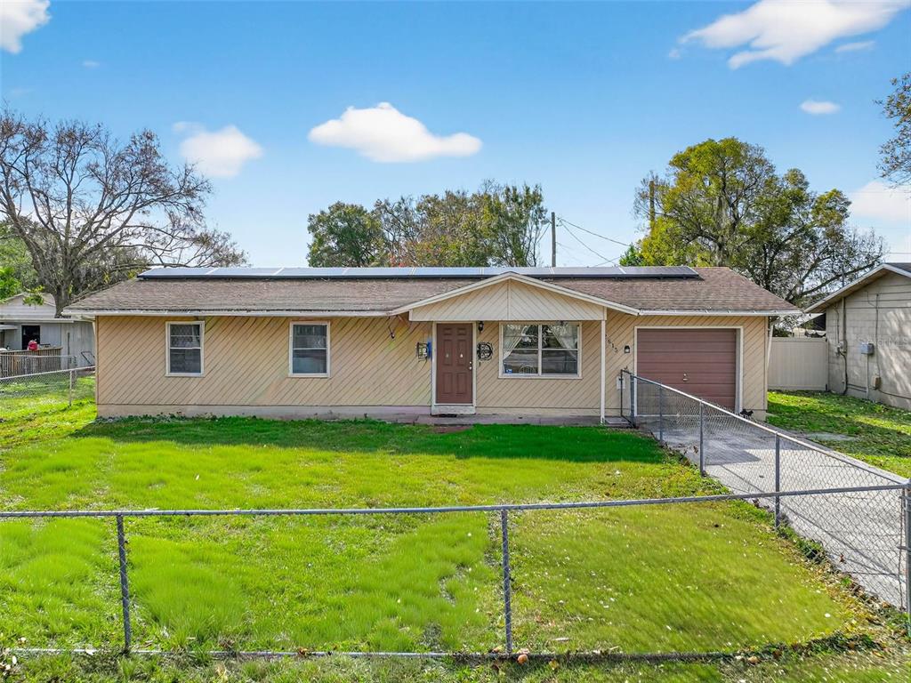 A single-story house with tan siding, a brown garage door, and solar panels on the roof — 2613 FOWLER AVENUE, AUBURNDALE, FL