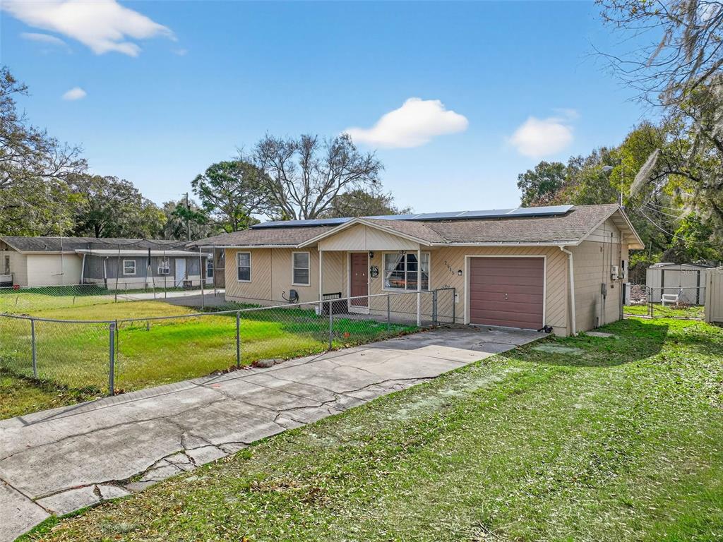 A tan, single-story house with a brown garage door, solar panels, and a chain-link fence — 2613 FOWLER AVENUE, AUBURNDALE, FL