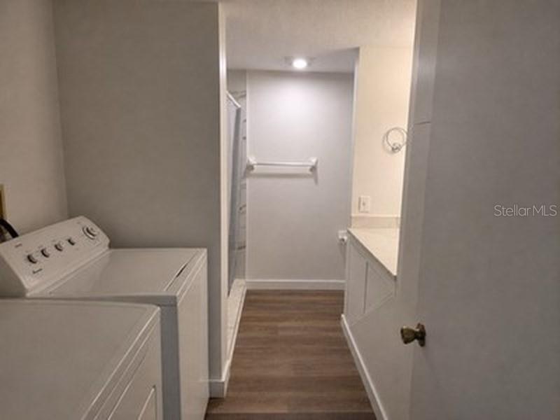 A laundry area with a white washing machine leads into a bathroom with wood-look flooring — 3425 HOLLAND DRIVE, BRANDON, FL
