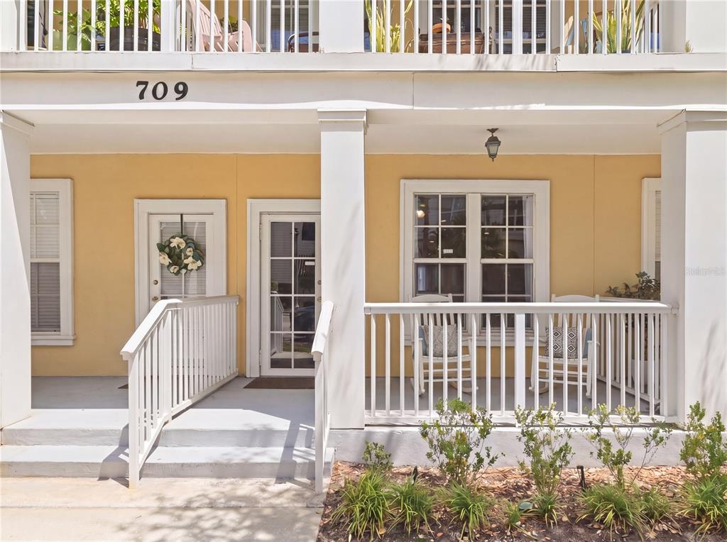 A yellow exterior porch features white railings, two glass-paned doors, and two rocking chairs — 709 BLOOM STREET UNIT 160, CELEBRATION, FL